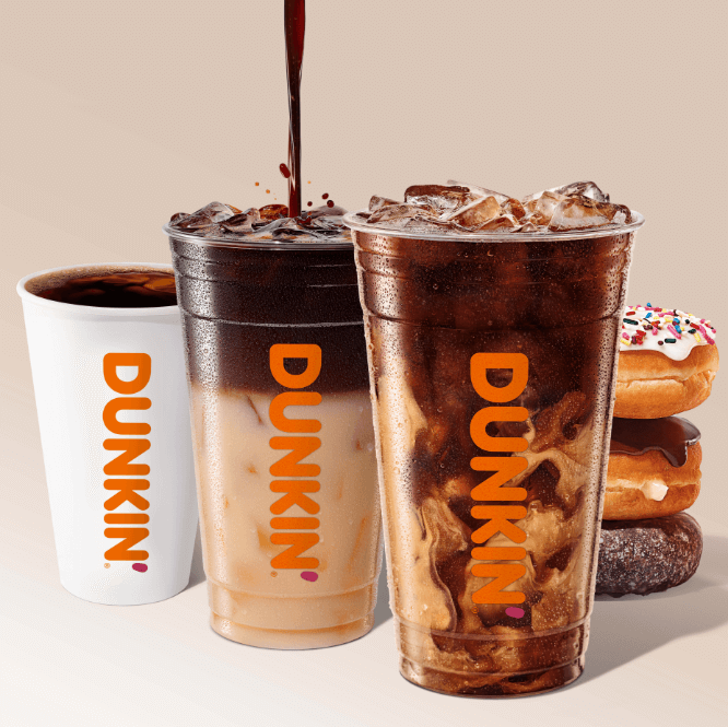 Pouring coffee into a Dunkin' iced coffee cup beside another full iced coffee and a hot coffee with stacked donuts at a coffee and donut franchise.