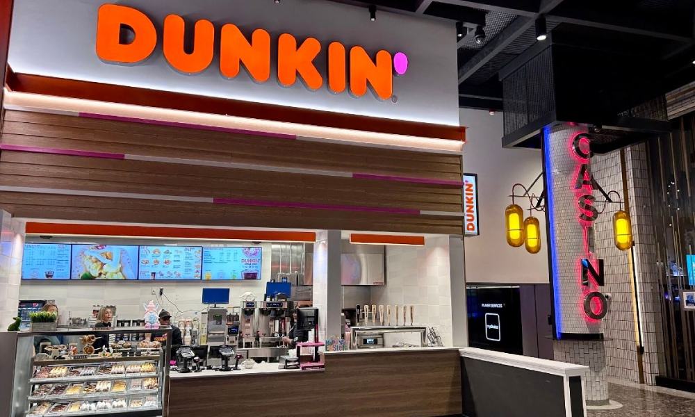 A Dunkin' store interior featuring a well-lit counter, menu screens, and a neon sign on the right, exemplifying a coffee and donut franchise.