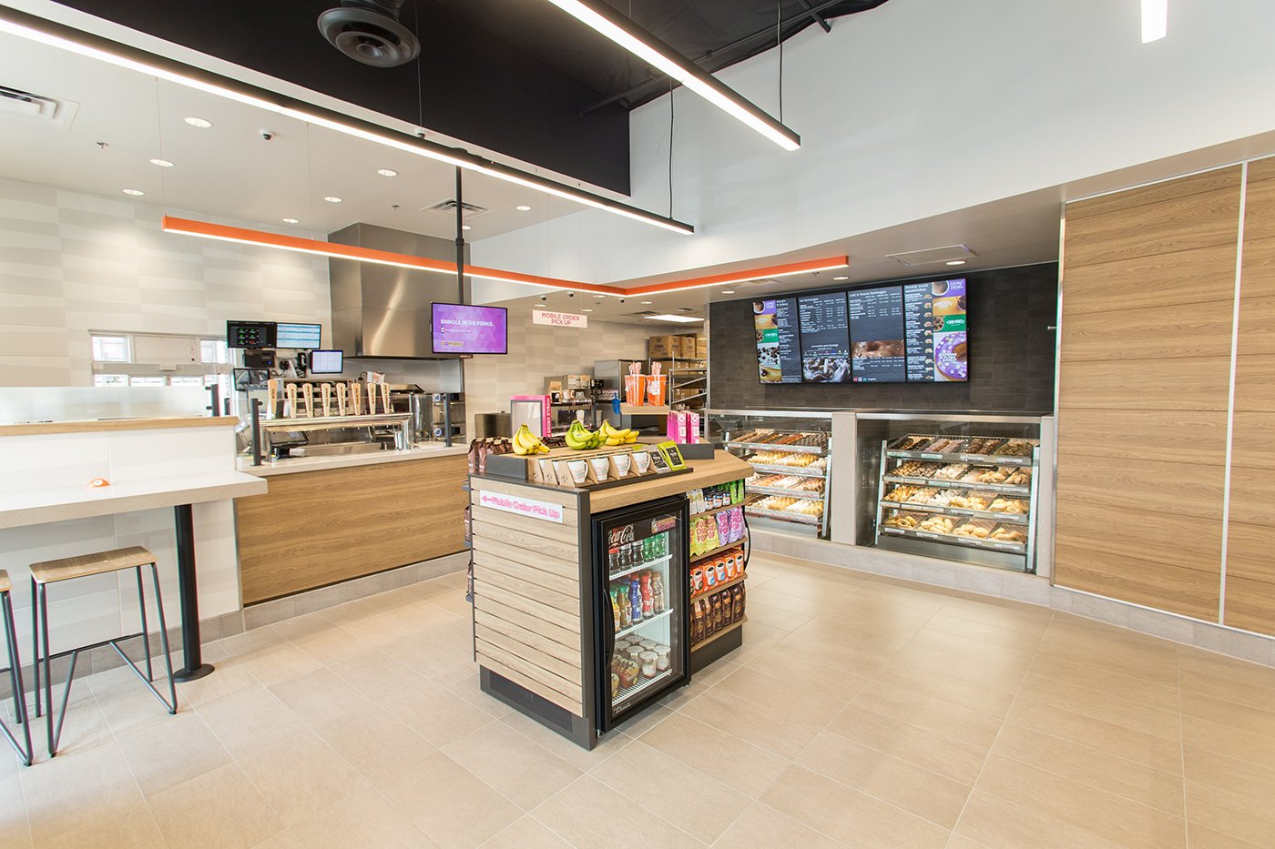 Modern coffee and donut franchise interior with digital menu boards, a beverage station, and a central food display.